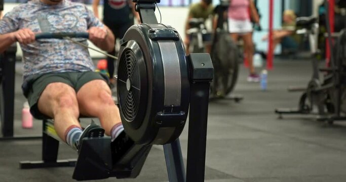 Male athlete on Rowing Machine in busy gym.