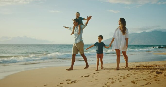 Happy young family walking on the beach together at sunset