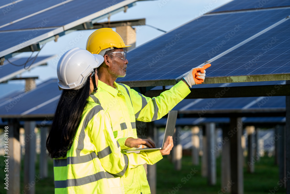 Poster two electrician workers in reflective vests and hard hats working at solar panels and talking about 