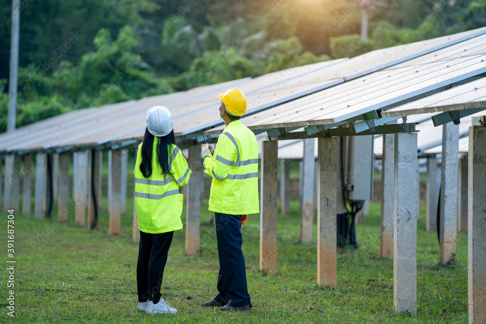 Poster two electrician workers in reflective vests and hard hats working at solar panels and talking about 