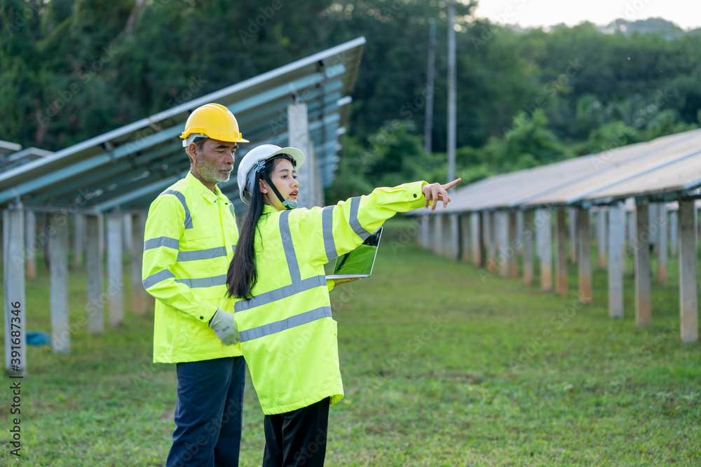 Poster Technician working with engineer planning new ecology project around field of solar panels.