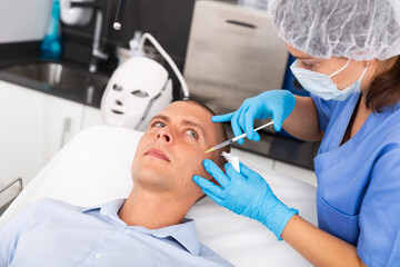Fototapeta premium Handsome young man receiving procedure of injection contouring for facial correction in cosmetology clinic