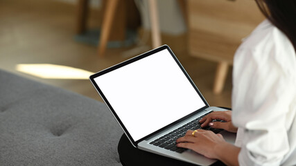 Cropped shot of woman freelancer hands typing on laptop with white screen while sitting on couch.