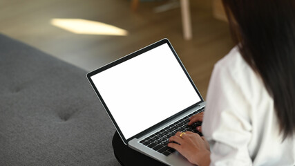 Cropped shot of calm female working on laptop and sitting on cozy sofa.