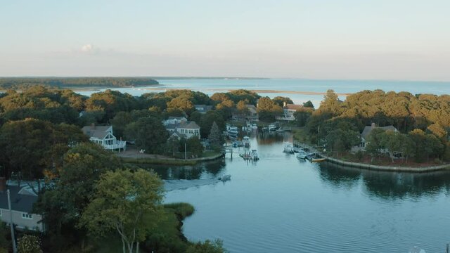 Cinematic low down aerial shot of a small speedboat passing through a private marina in Cape Cod during sunset. 4K Drone Shot