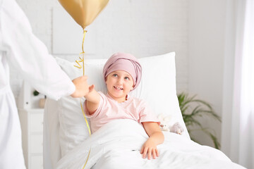 Doctor with golden balloon and little girl undergoing course of chemotherapy in clinic. Childhood...