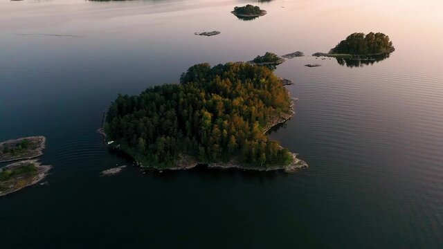 Aerial view towards a island, in the Stockholm archipelago, during a colorful, summer sunset, at the Baltic sea, in Sweden - tilt down, drone shot