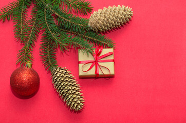 Natural spruce tree branch with a fir cone and Christmas decorations on a red background. Merry christmas and New Year. A minimalist composition, celebration and giving gifts. Copy space, flat lay.
