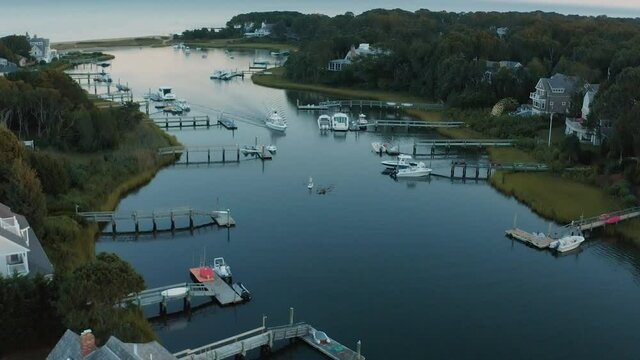 Low down aerial shot passing over a small speedboat and people wakeboarding through a private marina in Cape Cod during sunset. 4K Drone Shot