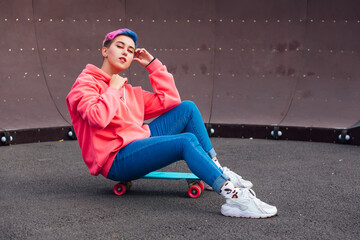 Stylish young woman sitting on her plastic skateboard in skatepark. Youth concept.
