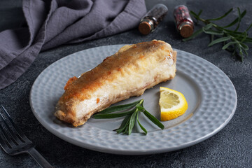 Fried fish hake Pollock and slices of fresh lemon. Dark concrete background. Copy space.
