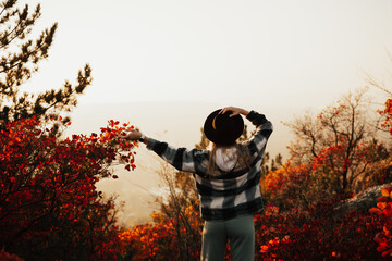 Autumn colourful photo of girl outdoors with black hat. Happy young girl enjoying the beauty of sunny day in autumn park. View from a back. Copy space.