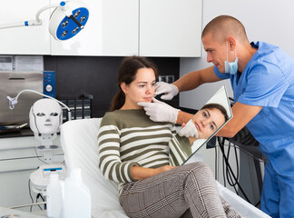 Young woman patient having consultation in aesthetic clinic, talking with confident man doctor