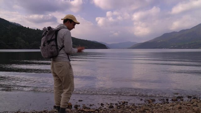 Male hiker skipping stone on beautiful lake in pristine nature setting
