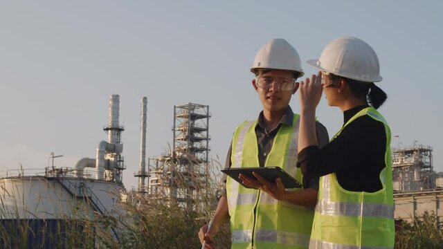 Medium shot. two Asian engineers using digital tablet working  and Talk, survey, for factory expansion outside at petroleum oil refinery in industrial estate