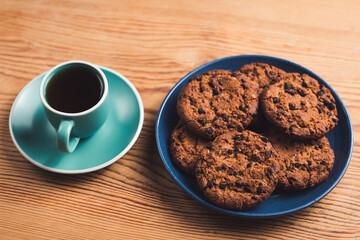 Chocolate oatmeal chip cookies on blue plate with green cup of coffee on wooden table. Concept of Breakfast or dessert.