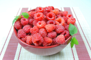   raw  fresh raspberries in a burgundy bowl on a wicker background    