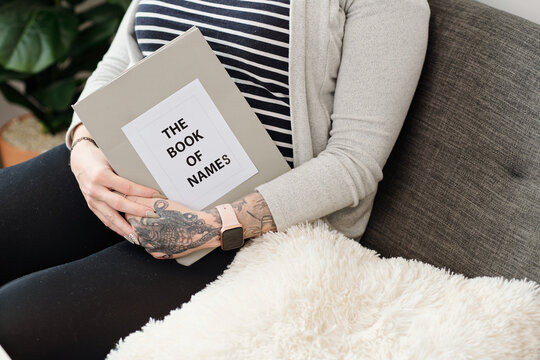 Cropped image of pregnant woman sitting on sofa with book of names