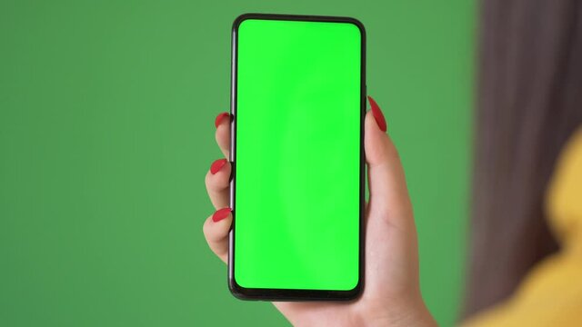 Woman hand holding the smartphone on green screen chroma key background. Mobile phone mock-up for your product. The iPhone Xr model in vertical orientation portrait mode