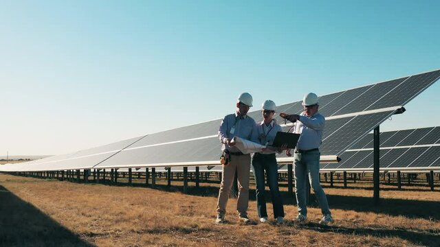 Team of three engineers working at solar farm. Solar power plant workers, solar energy industry concept.