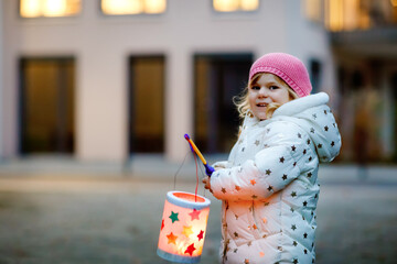 Fototapeta Little kid girl holding selfmade lanterns with candle for St. Martin procession. Healthy cute toddler child happy about children and family parade in kindergarten. German tradition Martinsumzug obraz