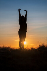 A woman reaches for the sky, stretching in the early morning light.