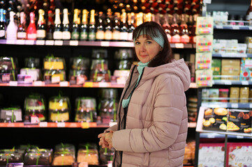 Photo of an adult Caucasian woman on the background of stalls with products in a shopping mall. The model is in outerwear.