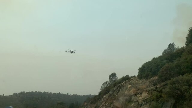 helicopter dropping water on large wildfire
