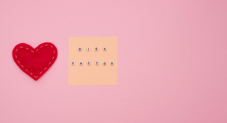 Concept of health, cardiology, heart disease. Words RISK FACTOR on white cubes, a heart made of fabric on a pink background. Flat lay, free space for text.