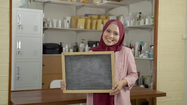 beautiful asian woman standing in front of her store holding blank black board