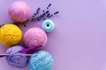 Flat lay of colored yarn balls for crocheting with lavender on a lilac background