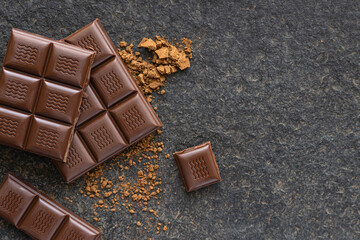 Broken pieces of chocolate and cocoa powder on a wooden background