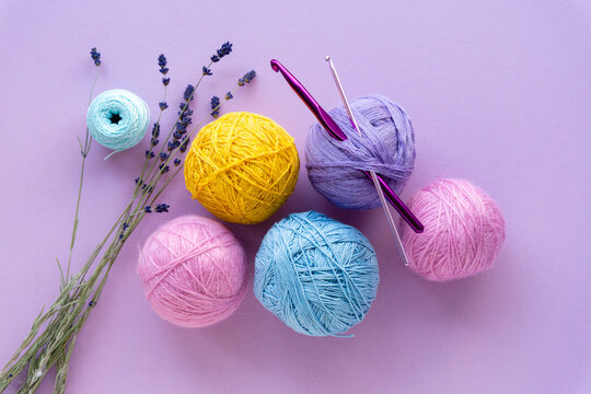 Flat lay of colored yarn balls for crocheting with lavender on a lilac background, top view