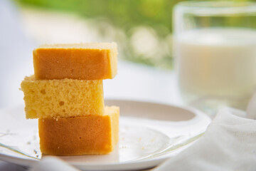 Close up a stack of butter cake on a white plate on a white table with a cup of milk blurred background.