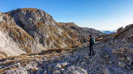 Fototapeta premium A panoramic capture of a woman hiking in Hochschwab region in Austrian Alps. The flora overgrowing slopes is turning golden. Autumn vibes in the mountains. Idyllic landscape. Freedom and wilderness