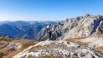 A panoramic capture of a man hiking in Hochschwab region in Austrian Alps. The flora overgrowing slopes is turning golden. Autumn vibes in the mountains. Idyllic landscape. Freedom and wilderness