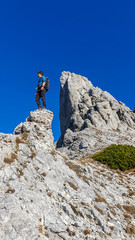 A man standing on top of a sharp, pointy rock formation in Hochschwab region, Austrian Alps. The steep mountain walls look very dangerous. High mountaineering. Autumn vibes in the mountains. Adventure
