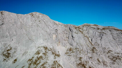 A panoramic view on a sharp and steep slopes of Hochschwab in Austrian Alps. The massive stony wall rockets up very steep. The flora overgrowing the slopes is turning golden. Autumn vibes. Wilderness