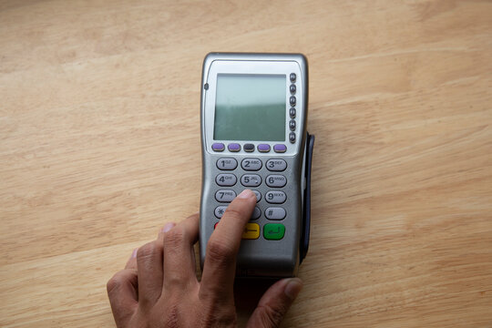 Male hand dials pin code on pin pad of card machine or pos terminal with inserted blank white credit