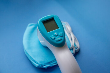 antibacterial medical mask of blue color on a blue background with thermometer gun 