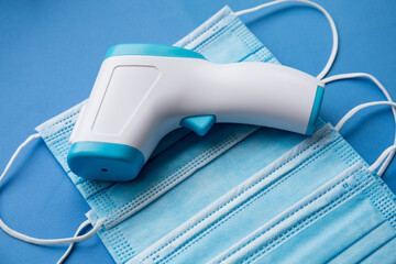 antibacterial medical mask of blue color on a blue background with thermometer gun 