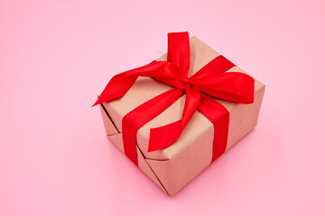Christmas or New Year gift box with red ribbon on against a pink background. Close-up, selective focus