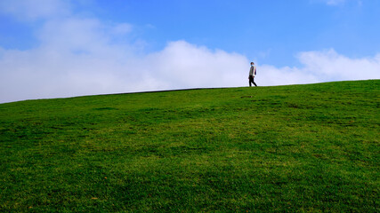 Woman with medical mask walking on a green hillside under blue sky