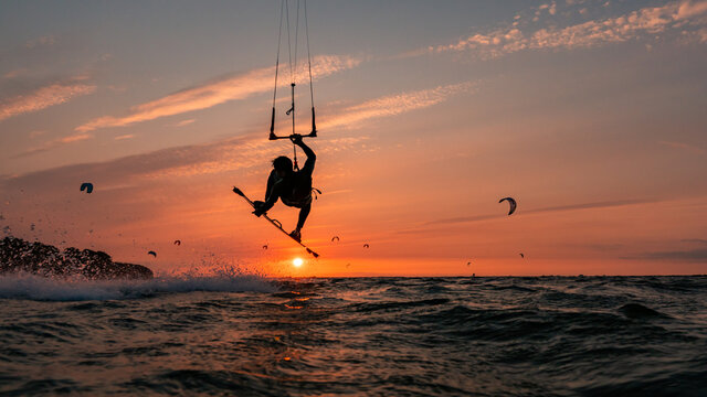 Silhouette of kitesurfer jumping with grab in the orange sunset at the baltic sea