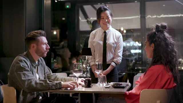 Waitress welcoming and taking food order from a cool fellow couple in an Asian restaurant. Young boyfriend and girlfriend ready to order.
