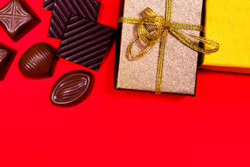 Black and milk chocolate and candy in gift boxes on a red background with a place for text. Sweet gifts, banner for confectionery