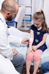 Fototapeta premium Pediatrician bandaging child hand in hospital office during medical examination. Healthcare physician specialist in medicine providing health care services treatment consultation .