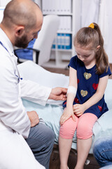 Pediatrician bandaging child hand in hospital office during medical examination. Healthcare physician specialist in medicine providing health care services treatment consultation .