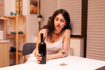 Alcoholic woman holding bottle of wine being depressed. Unhappy person disease and anxiety feeling exhausted with having alcoholism problems.