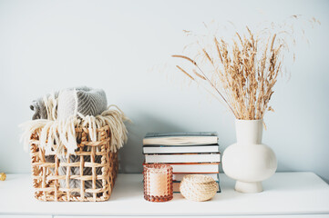 cozy modern interior details with fluffy reeds, candles and books in beige tones. Minimalist nordic...